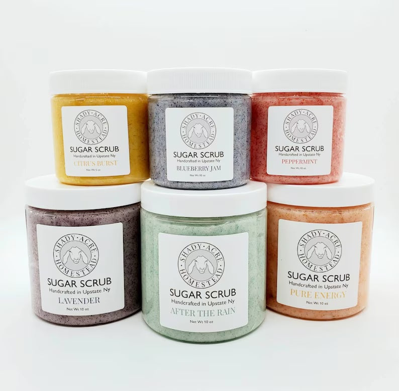 Five jars of handmade sugar scrub in various scents and colors stacked in a pyramid arrangement.