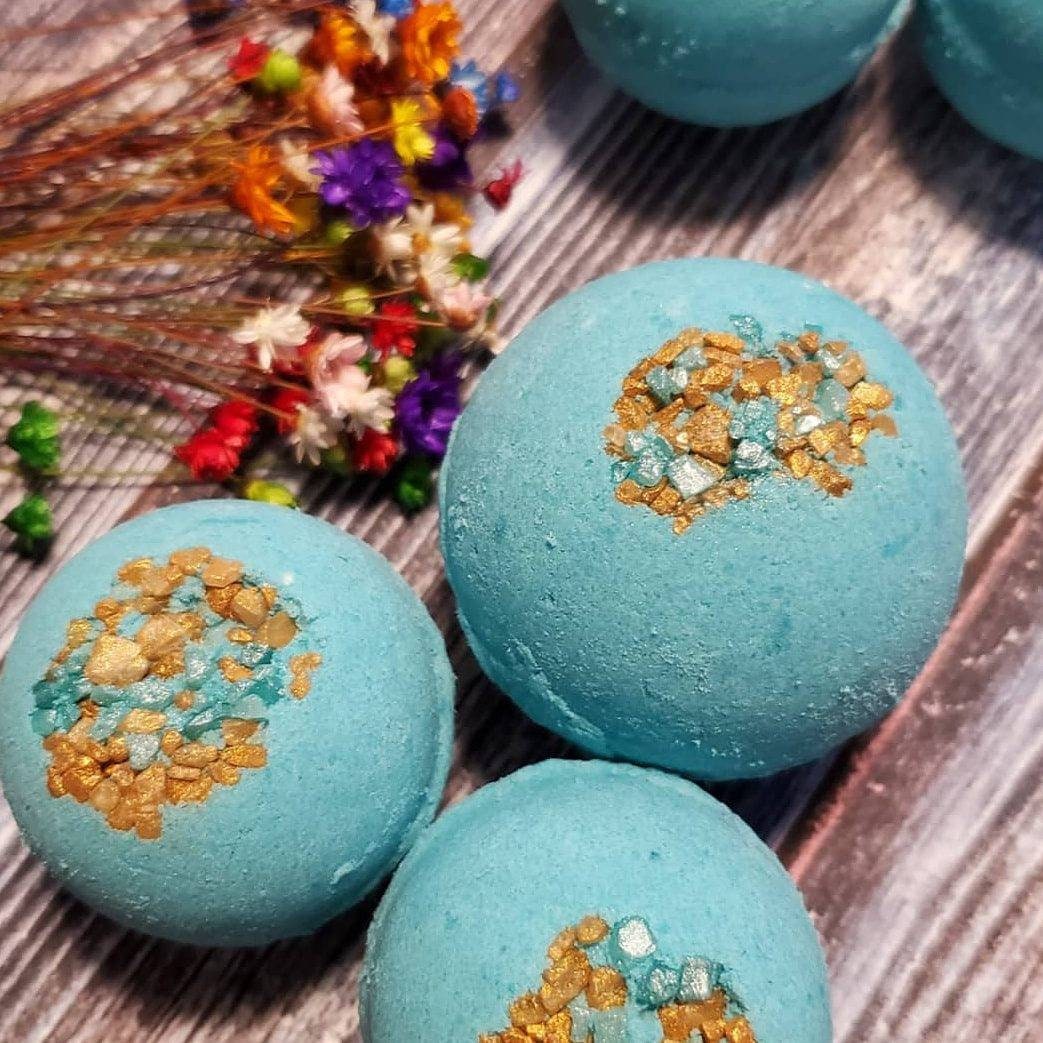 Blue bath bombs with gold and turquoise embellishments on a wooden surface with dried flowers nearby.