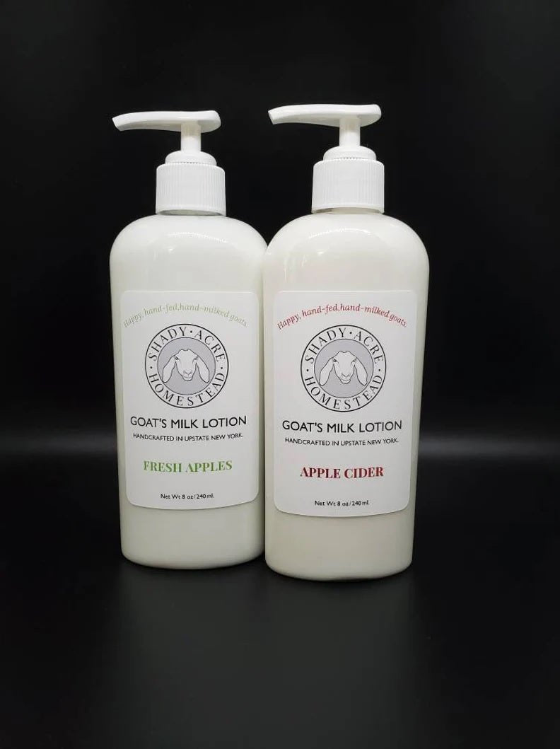 Two bottles of goat's milk lotion labeled Fresh Apples and Apple Cider on a dark background.